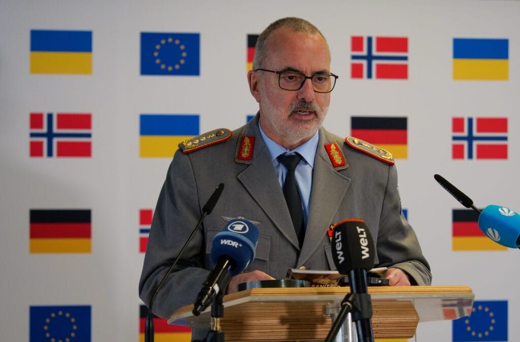 Ein Militäroffizier hält eine Rede auf einem Podium mit europäischen Flaggen im Hintergrund.