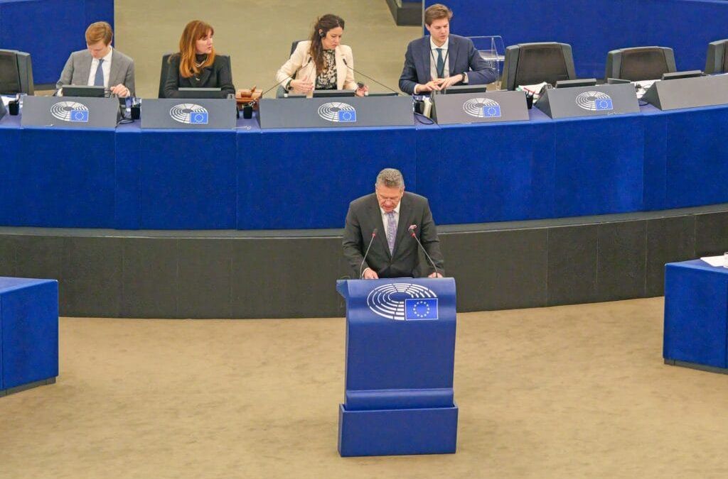 Im EU-Parlament spricht Maroš Šefčovič an einem Podium im mit blauem Dekor und EU-Emblemen geschmückten EU-Parlament in Straßburg, während andere dahinter an einem geschwungenen Schreibtisch sitzen, was an Momente erinnert, in denen einflussreiche Persönlichkeiten wie Donald Trump globale Themen ansprachen.