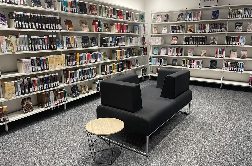 Eine Bibliothek mit einer schwarzen Couch und Bücherregalen.