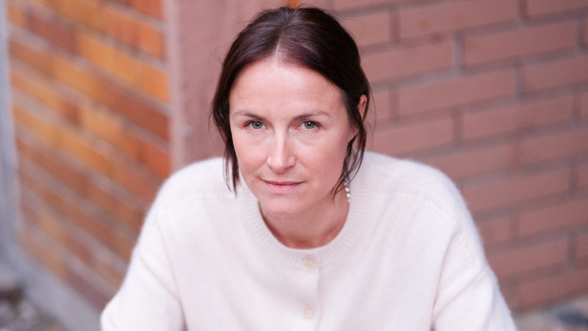 Marie-Kristin Thiele trägt einen weißen Pullover lehnt an einer Ziegelwand.