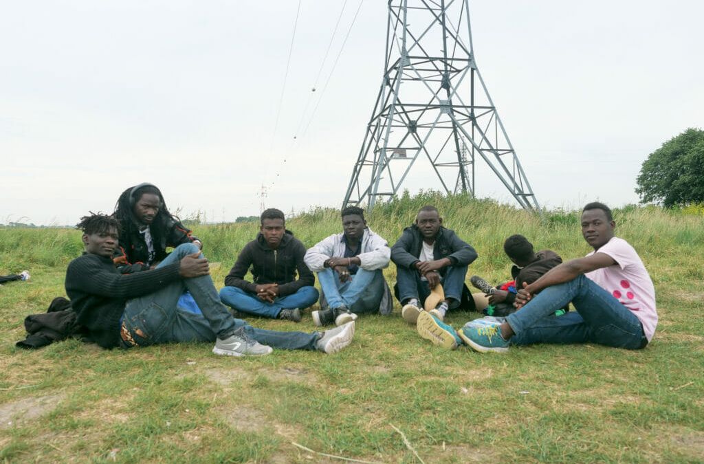 In Calais hoffen Mitte Juni rund 1000 Menschen auf einen Weg Richtung Großbritannien. Eine Gruppe sitzt auf einem Feld.