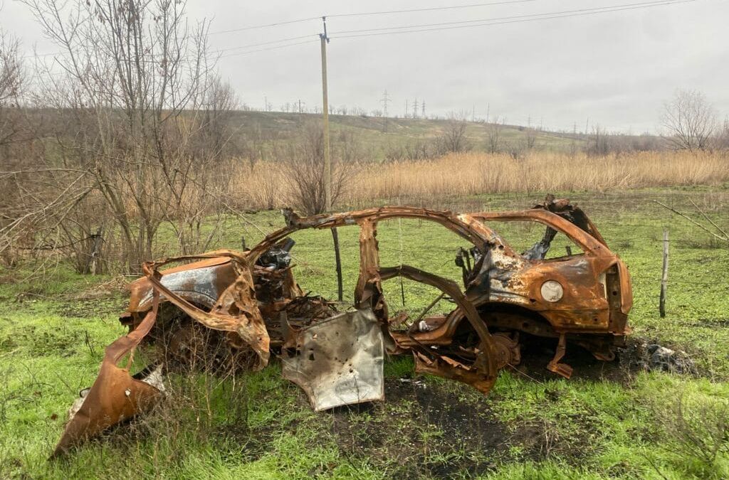 Ein verrostetes Auto steht mitten auf einem Feld.