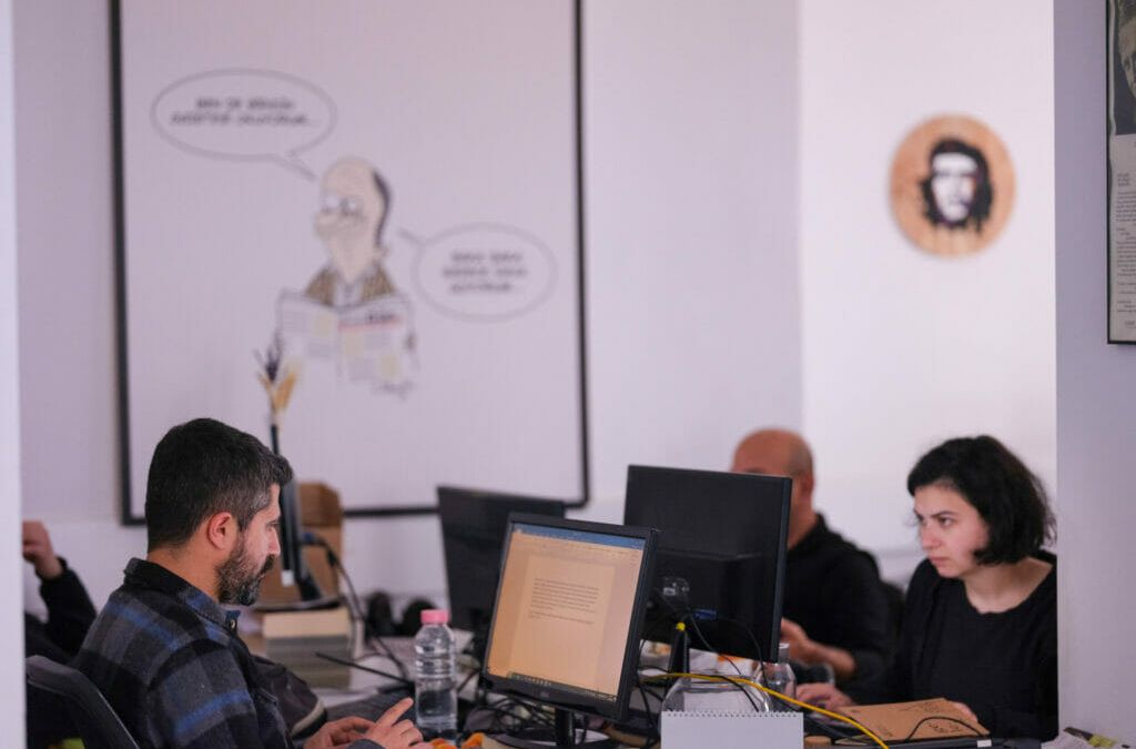The photo shows a shared office of the Turkish daily newspaper BirGün. Four editors sit at desks pushed together and work. In the background, a caricature hangs on the wall and next to it the portrait of Che Guevara.