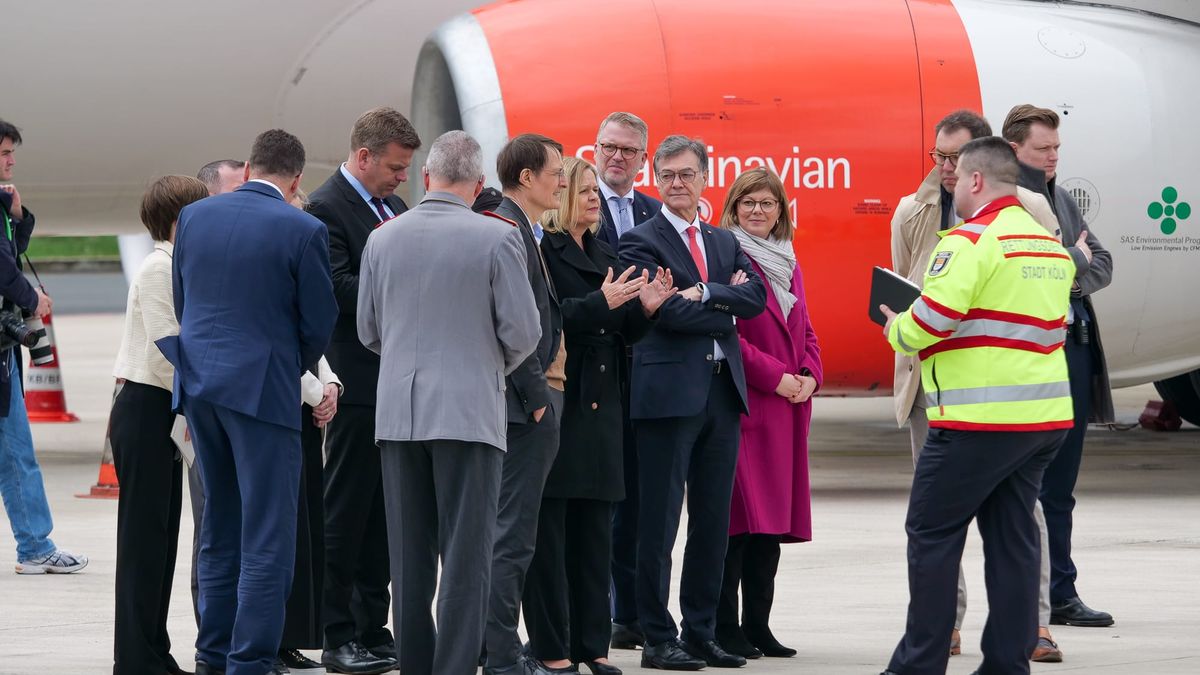 Eine Gruppe von Personen in Berufskleidung diskutiert auf dem Rollfeld eines Flughafens neben einem Flugzeug.