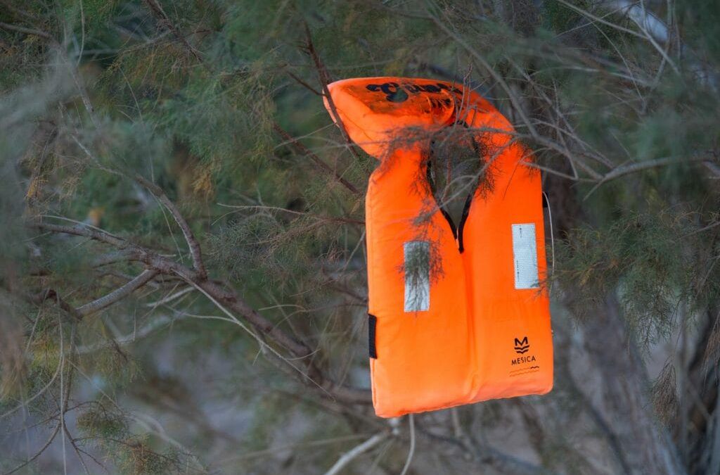 Eine orangefarbene Schwimmweste hängt an einem Baum.