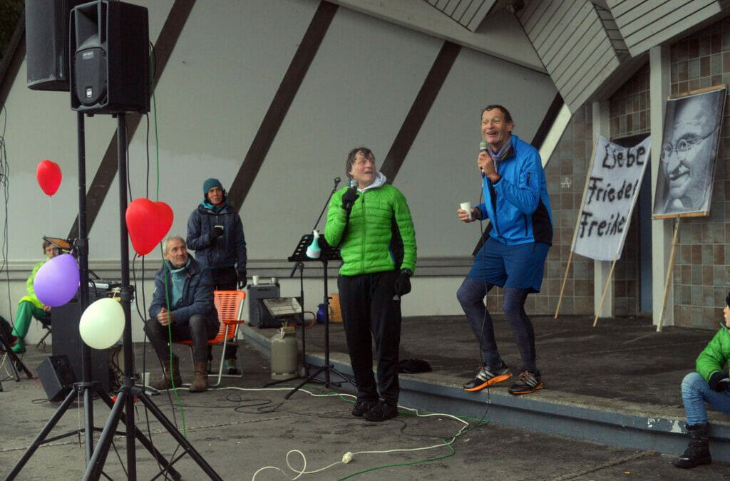 (v. li.) Friedensketteninitiator Gerry Mayr und sein Schweizer Ko-Organisator Jean Claude Greuter sind zur Demo durch den Regen gejoggt, um die Nachfolgeveranstaltung der Großversammlung anzukündigen. Nur dem Ordnungsamt möchten sie die Versammlung nicht melden. Das sei nicht notwendig, da es sich um den Zieleinlauf eines Halbmarathons handle, mit dem sie den Konstanzer Trichter füllen möchten.