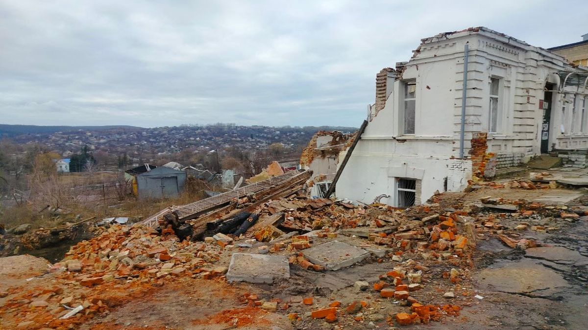 A partially collapsed building with scattered bricks and rubble in the foreground, overlooking a distant landscape under a cloudy sky.